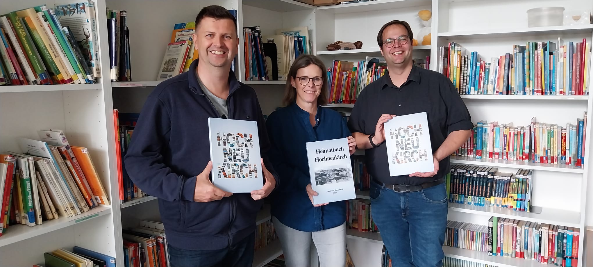 A. von Blumenthal, A.Pinter, B.Obst stehen nebeneinander in der Grundschulbücherei und halten das Heimatbuch in ihren Händen
